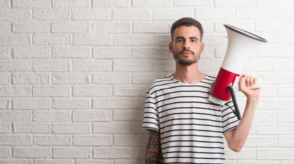Young adult man holding megaphone with a confident expression on smart face thinking serious