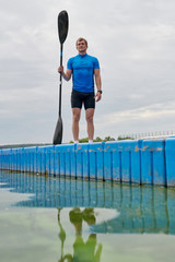 Young sportsman in sportswear standing on pier with paddle, he is ready for kayaking