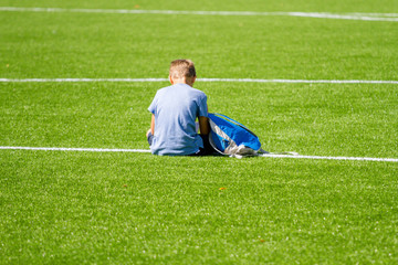 Sad alone boy with backpack sitting stadium outdoors