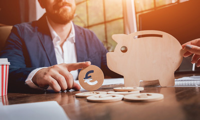 Businessman holds a coin near wooden piggy. Money box. Collecting money with earning bank.