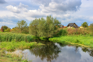 Fototapeta na wymiar View of village pond against gray sky with clouds on a summer morning