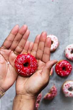Hand Holding homemade fresh mini red frosted Donut with sprinkles, selective focus
