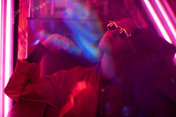 Long hair girl with sunglasses and leather jacket looking at neon lights