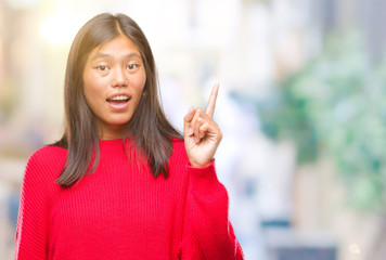 Young asian woman wearing winter sweater over isolated background pointing finger up with successful idea. Exited and happy. Number one.