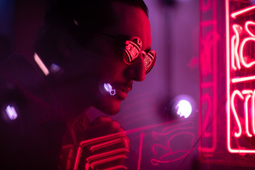 man with stubble and sunglasses looking at neon sign