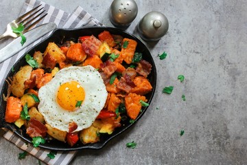 Skillet Breakfast Hash with potatoes bacon  peppers sweet potatoes and fried egg, top view