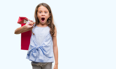 Brunette hispanic girl holding shopping bags scared in shock with a surprise face, afraid and excited with fear expression