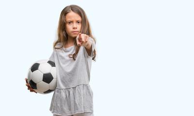 Brunette hispanic girl holding soccer football ball pointing with finger to the camera and to you, hand sign, positive and confident gesture from the front