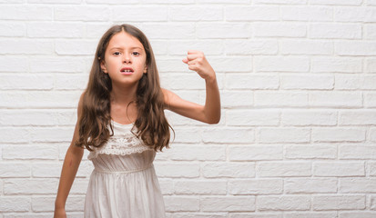 Obraz na płótnie Canvas Young hispanic kid over white brick wall angry and mad raising fist frustrated and furious while shouting with anger. Rage and aggressive concept.