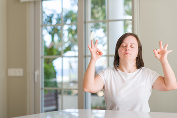 Down syndrome woman at home relax and smiling with eyes closed doing meditation gesture with fingers. Yoga concept.