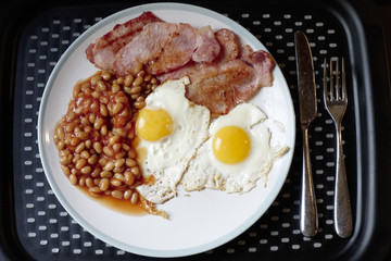 Fried breakfast view from above of bacon beans and eggs on plate and tray