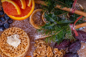 Fototapeta na wymiar Toasted Crumpets with Butter. Warm toasted Crumpets with Butter on a chopping board with a selection of dried fruit and nuts. Surrounded by Christmas presents and gifts.