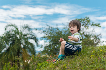 a boy sitting on the grass holding a small flower in his hand