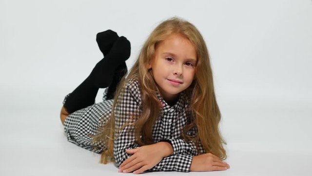 A girl in a checkered dress lies on the floor, gently smiling at the camera. 