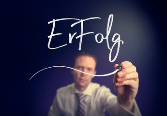 A businessman writing a Success "Erfolg" concept in German with a white pen on a clear screen.