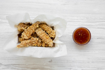 Chicken strips in paper box with sweet chili sauce on a white wooden background, overhead. Flat lay, top view, from above. Closeup.