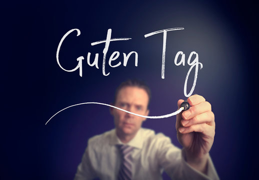 A businessman writing a Good Day "Guten-Tag" concept in German with a white pen on a clear screen.