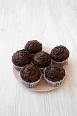 Chocolate cupcakes on pink plate on white wooden table, high angle view.