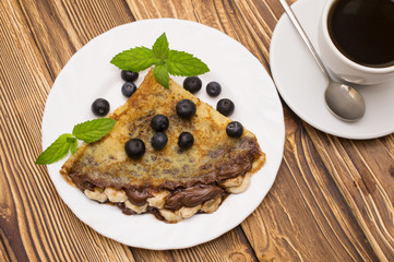 Homemade crepes served with fresh blueberries and powdered sugar on rustic wooden table in cast iron skillet