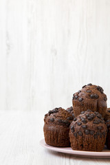 Chocolate cupcakes on pink plate on white wooden background, side view. Close-up. Copy space.