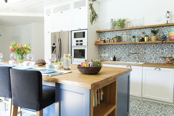 Stylish and sunny kitchen interior with accessories, wooden table and plants. Design space. 