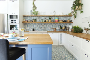 Stylish and sunny kitchen interior with accessories, wooden table and plants. Design space. 