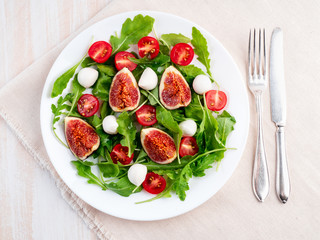 Fresh salad with figs, tomatoes, cucumbers, arugula, mozzarella. Oil with spices, top view, white background