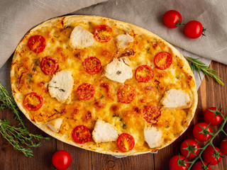 Appetizing golden focaccia with tomatoes, chiken meat, spices on dark wooden rustic table, top view
