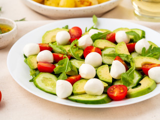Fresh salad with tomatoes cucumbers arugula mozzarella and avocado. Oil with spices rosemary thyme, side view close up