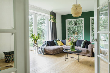 Stylish interior with sofa, colors pillows, flowers and wooden floor. Sunny and bright living room...