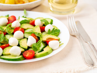 Fresh salad with tomatoes cucumbers arugula mozzarella and avocado. Oil with spices rosemary thyme, side view