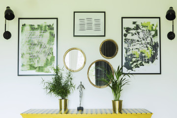 Sunny and bright living room with design commode, photo frames and plants. 