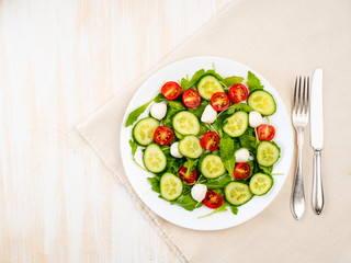 Fresh salad with tomatoes, cucumbers, arugula, mozzarella. Oil with spices, top view, white background, copy space