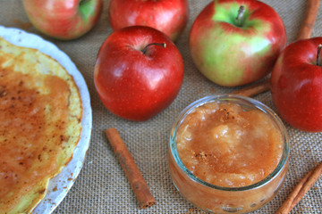 Apple marmalade with cinnamon in a jar, apples in the background, cinnamon sticks and pancake