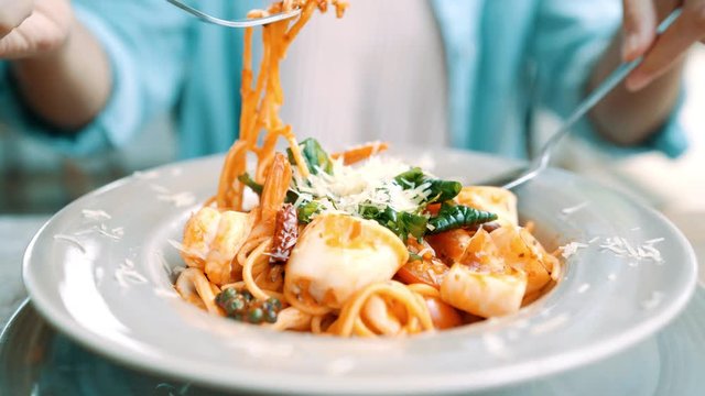 Beautiful Happy Asian Woman Eating A Plate Of Italian Seafood Spaghetti At Restaurant Or Cafe While Smiling And Looking At Food.