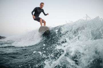 Blue wave in focus on a foreground with a man wakesurfing down it on the background