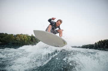Wakeboarder jumping on the blue wave against the background of clear sky