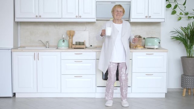 Happy Elderly Woman Dancing In Kitchen. Funny Grandmother.