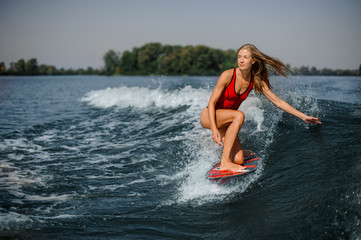 Attractive blonde woman wakesurfer riding down the blue splashing wave