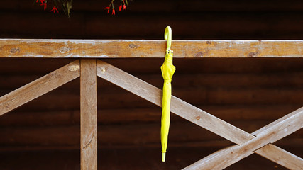 Желтый зонтик висящий на деревянных перилах дома - obrazy, fototapety, plakaty