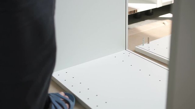 Erector assembling shelves at home. Furniture foreman puts white board to the metal pintles in the other one to fix the furniture. Indoors.
