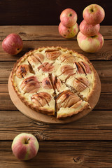 Homemade apple pie with cream filling served with organic apples on old wooden background