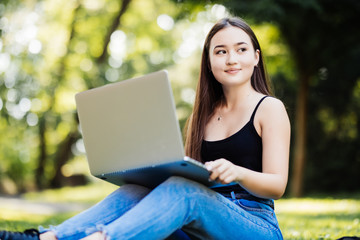 Japanese student working on her laptop while laying on grass on green background