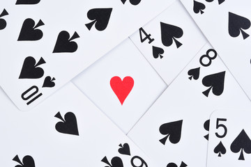 Black Playing Cards scattered on a table with a single red heart exposed