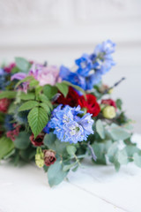 selective focus. Elongated floral arrangement in vintage metal vase. table setting. Blue and red color. Gorgeous bouquet of different flowers. Bright room, stucco on the wall