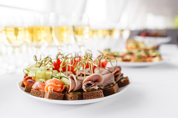 rye bread sandwiches, canapes, bruschetta on white plate. solemn banquet. Lot of glasses champagne or wine on the table in restaurant. buffet table with lots of delicious snacks.