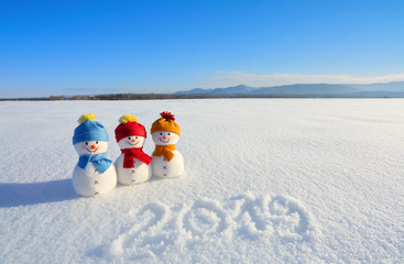 2019 written on the snow. Smiling snowman with hats and scarfs are standing on the field with snow....