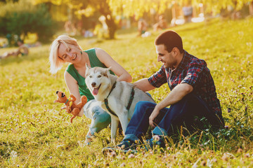 Dog with owners spend a day at the park. Young couple and husky running, playing and having fun.