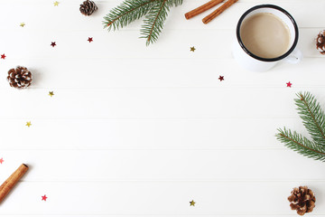 Christmas composition. Frame made of fir, spruce branches, pine cones, cinnamon sticks and glittering confetti stars on white wooden table background. Coffee in enamel mug. Flat lay, top view.