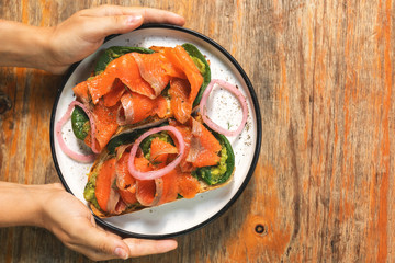 Female hands and delicious toasts with a smoked salmon, avocado and basil leaves